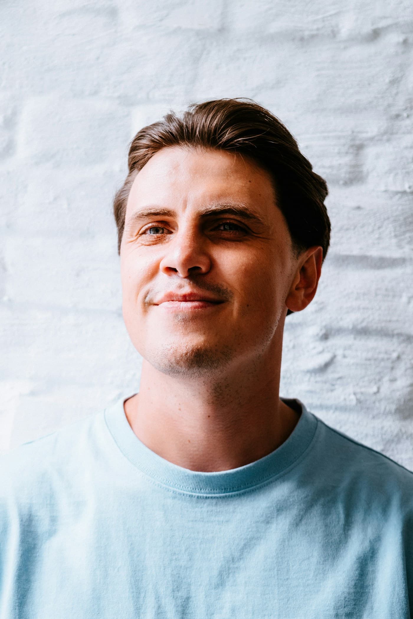 Natural portrait of a smiling man in a light blue T-shirt against a whitewashed brick wall